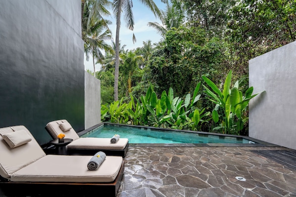 A poolside area with lounge chairs and a small table, surrounded by lush greenery and a clear pool. - Emana Lumina (Ubud)
