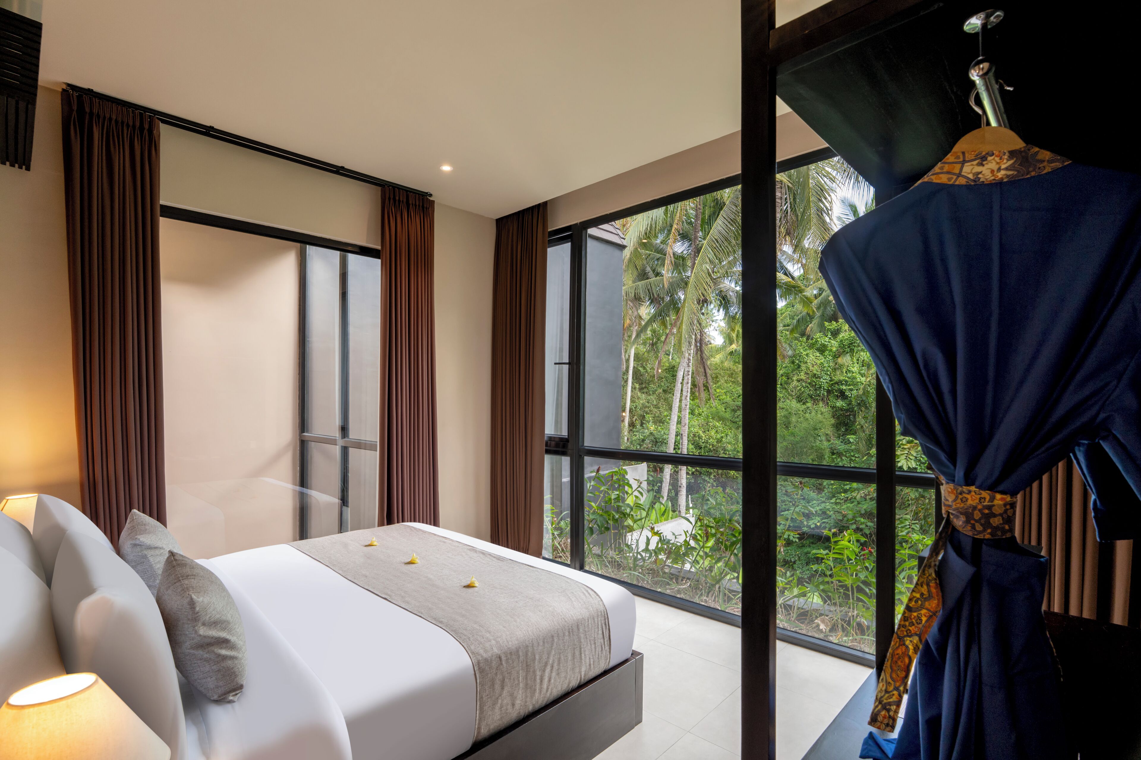 Un dormitorio moderno con una cama grande, cortinas y vistas a un paisaje tropical.
