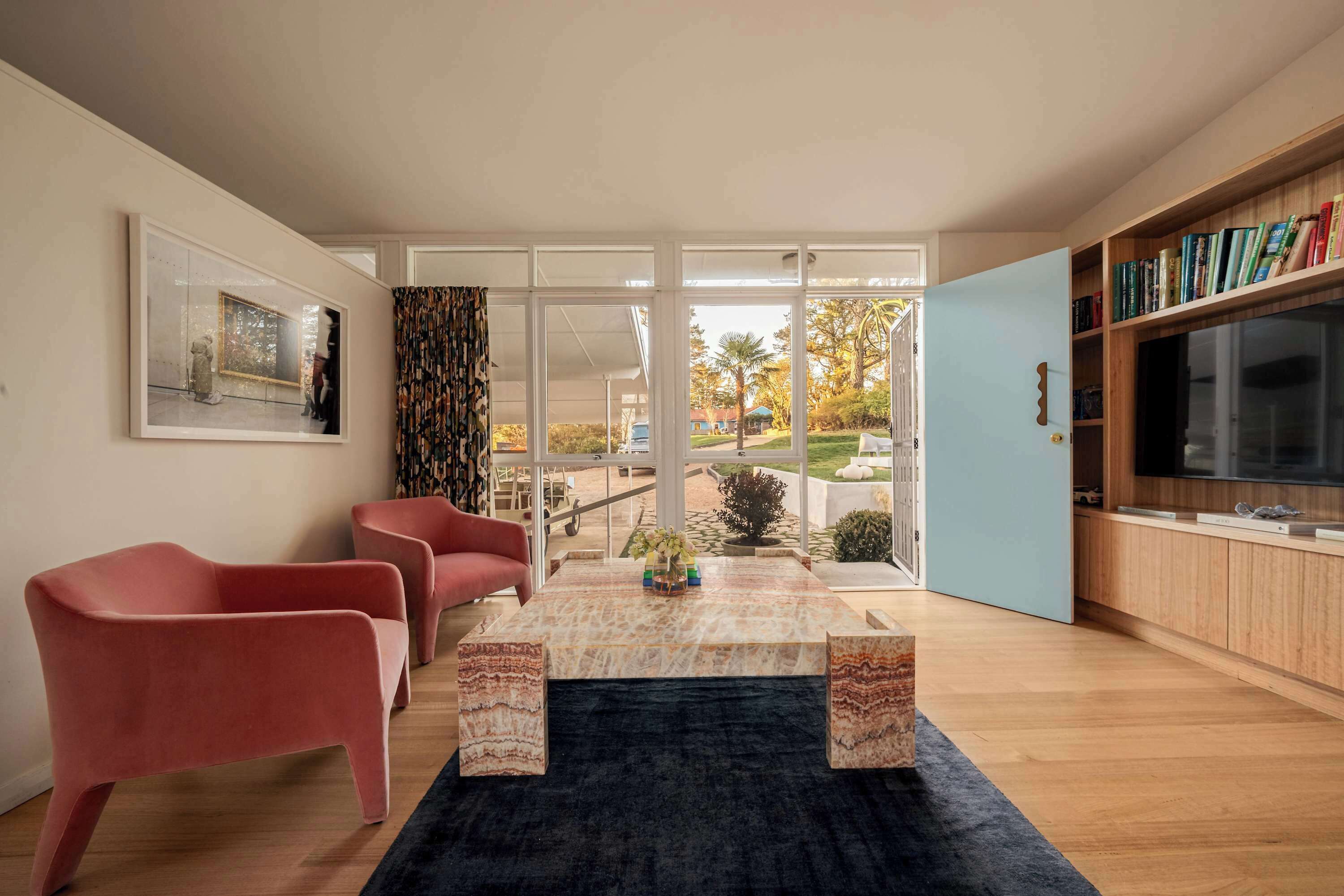A modern living room with a glass door leading to a garden, a flat-screen TV, and a bookshelf.