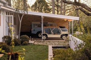 A vehicle parked under a covered area with a brick wall and a house in the background. - Sol Haus | Hot Tub, Volleyball & Fireside Nights (Wentworth Falls)