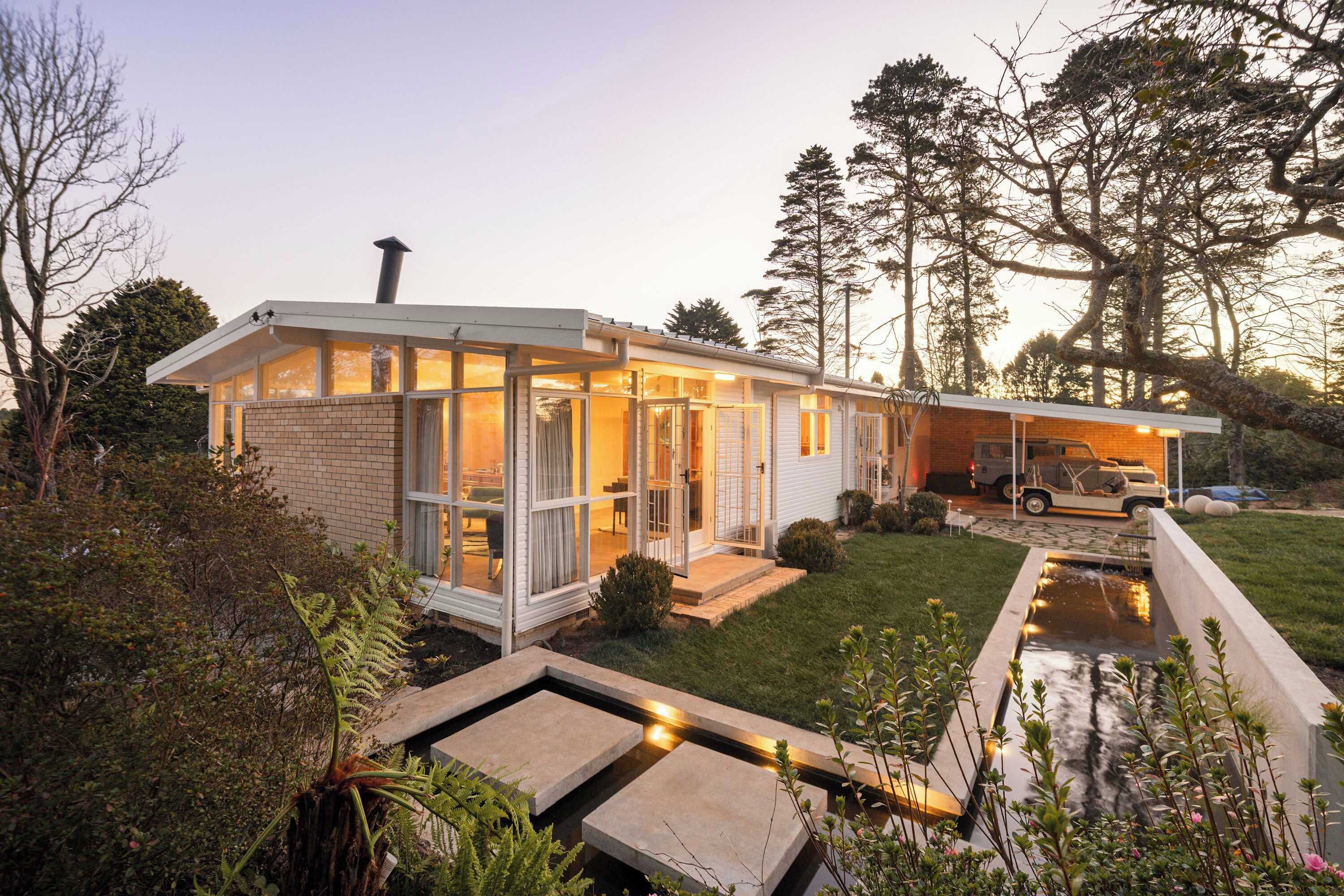 Une maison moderne avec une façade en briques, de grandes fenêtres et un petit jardin à l’avant agrémenté d’un élément décoratif aquatique.