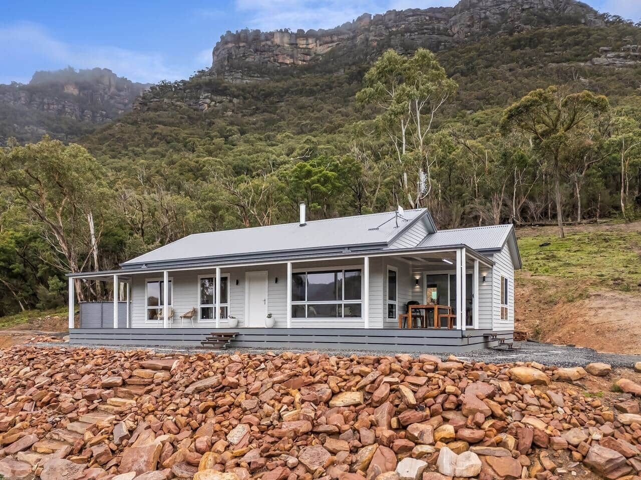 Une maison de plain-pied dotée d’un porche abrité, entourée d’un grand amas de rochers.