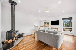 Ein modernes Wohnzimmer mit Kamin, grauem Sofa, Holzböden, Deckenventilator und Wand-Fernseher.