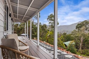 A covered outdoor area with a wooden deck, wicker chairs, and a view of a mountainous landscape. - House on the Rock | Brand New with stunning views (Halls Gap)