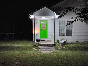 Uma casa com porta verde, varanda e um pequeno galpão com churrasqueira.