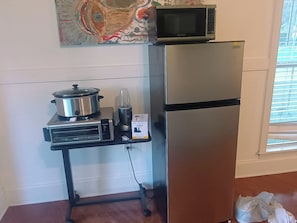 A kitchen with a stainless steel refrigerator, a microwave, a slow cooker, and a blender on a small countertop.