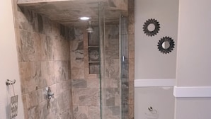 A bathroom with a glass-enclosed shower, stone tiles, a toilet, and a vanity with a sink.