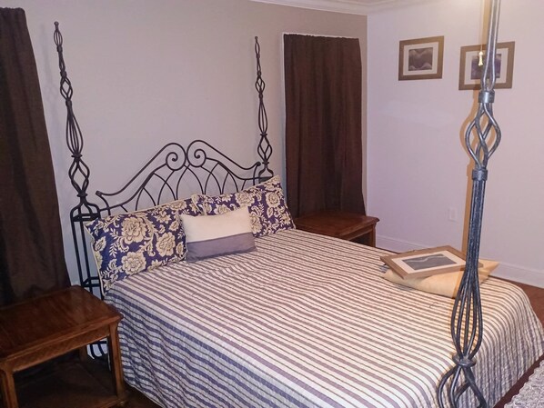 Een slaapkamer met een hemelbed, twee nachtkastjes, een kaptafel, een houten dressoir en een aan de muur bevestigd fotolijstje.