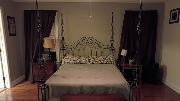 A bedroom with a four-poster bed, a bedside table with a lamp, a nightstand, and a bench.