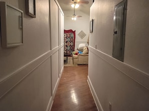 A narrow hallway with a wooden floor, a ceiling fan, and a door on the right.