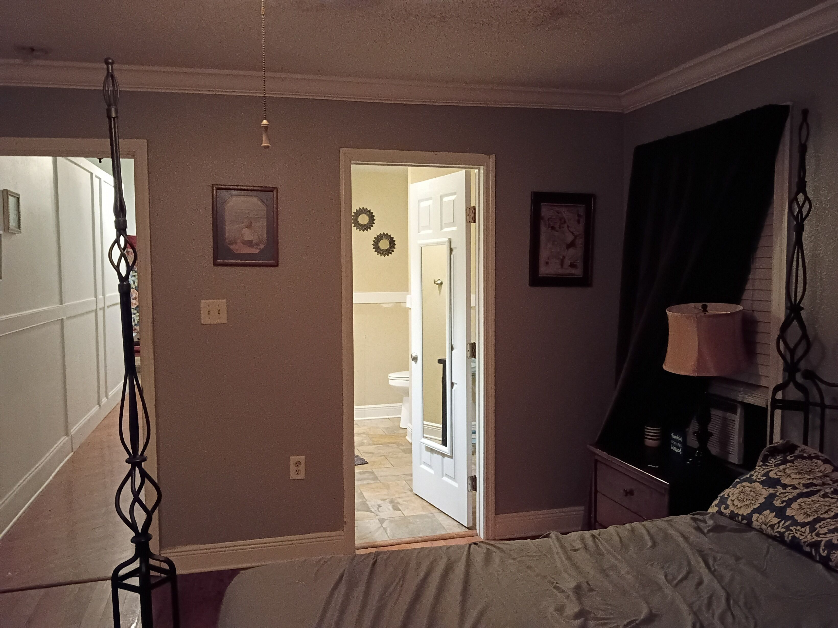 A bedroom with a bed, a nightstand, a lamp, and a door leading to a bathroom.