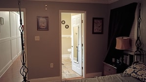 A bedroom with a bed, a nightstand, a lamp, and a door leading to a bathroom.