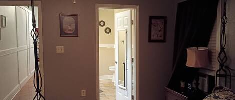 A bedroom with a bed, a nightstand, a lamp, and a door leading to a bathroom.