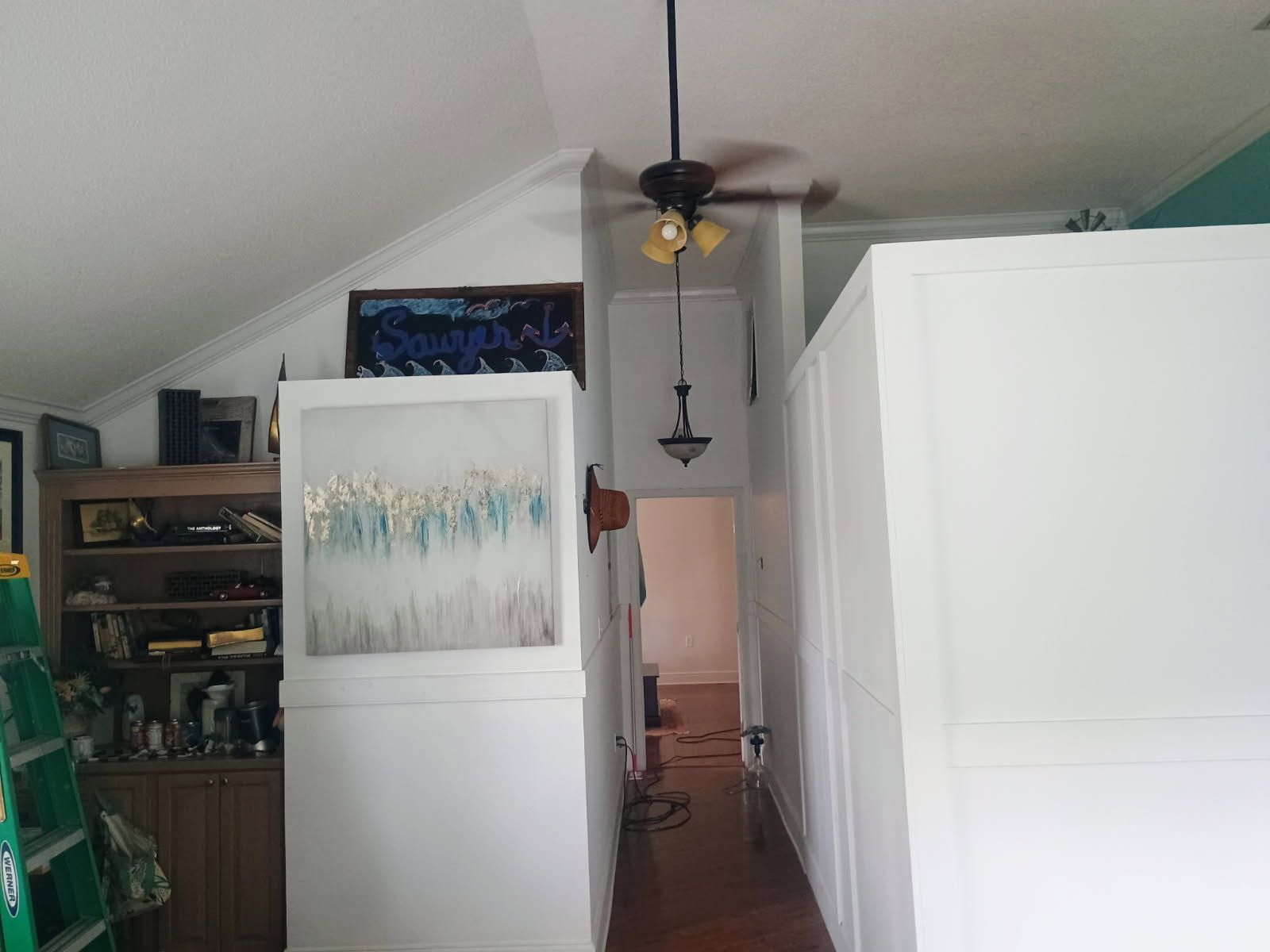 A hallway with a white refrigerator, a ceiling fan, and a sign on the wall.