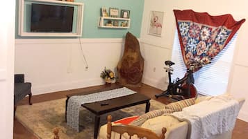 Uma sala de estar com televisão, mesa de centro de madeira, sofá e mesa de jantar com cadeiras.