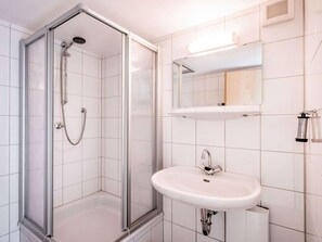 Een moderne badkamer met een douchecabine van glas, een witte wastafel en een spiegel erboven.