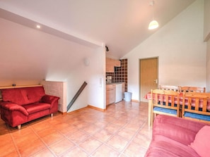 Een ruime woonkamer met een rode bank, een eettafel met stoelen en een keuken op de achtergrond.