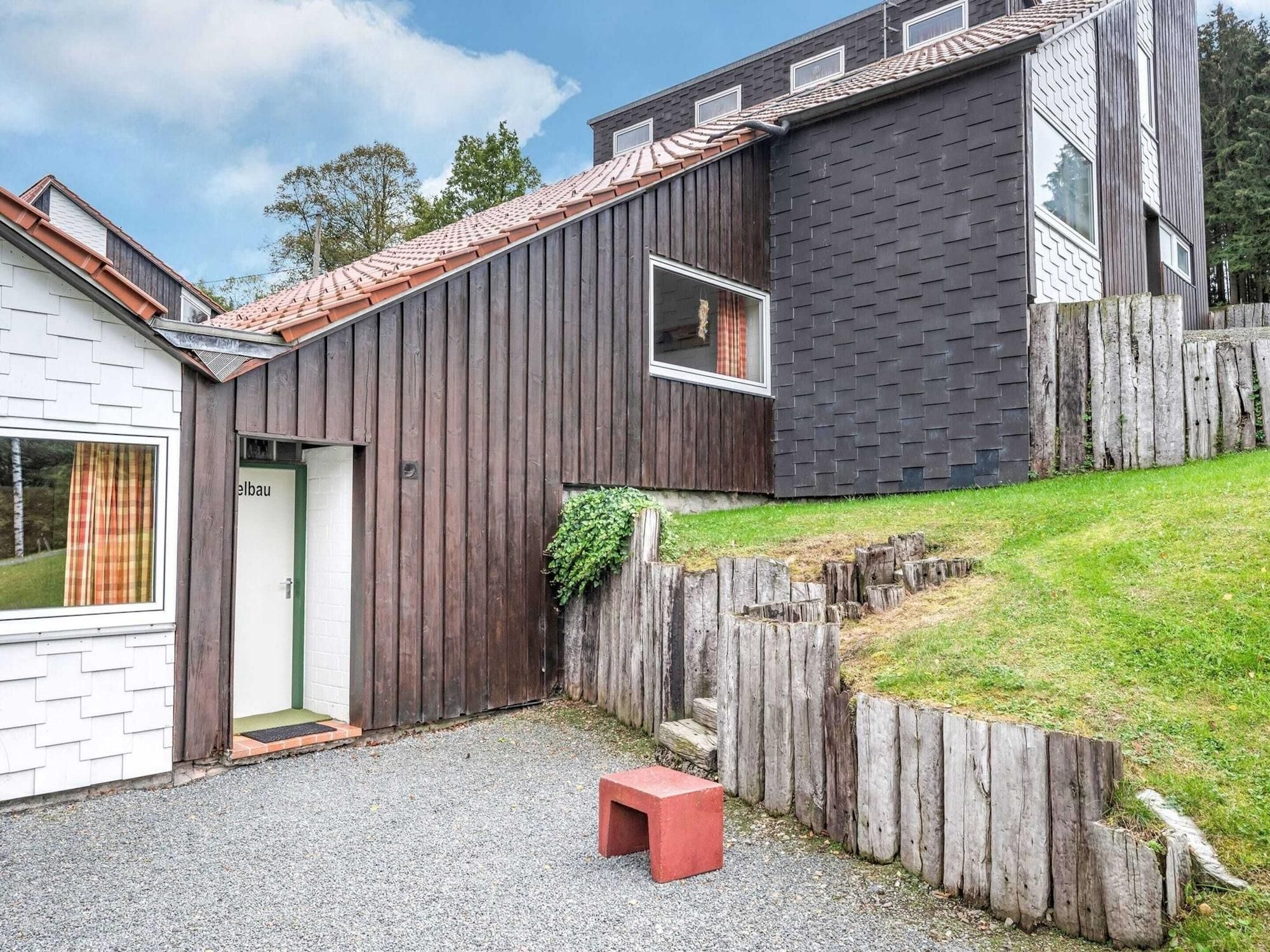 Una casa moderna con fachada de madera, camino de grava y un taburete rojo pequeño.