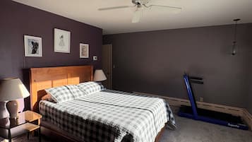 A bedroom with a bed, a ceiling fan, a treadmill, and wall art.