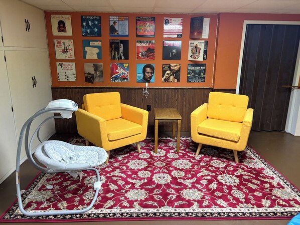 A room with two yellow armchairs, a small wooden table, a white massage chair, and a red patterned carpet.