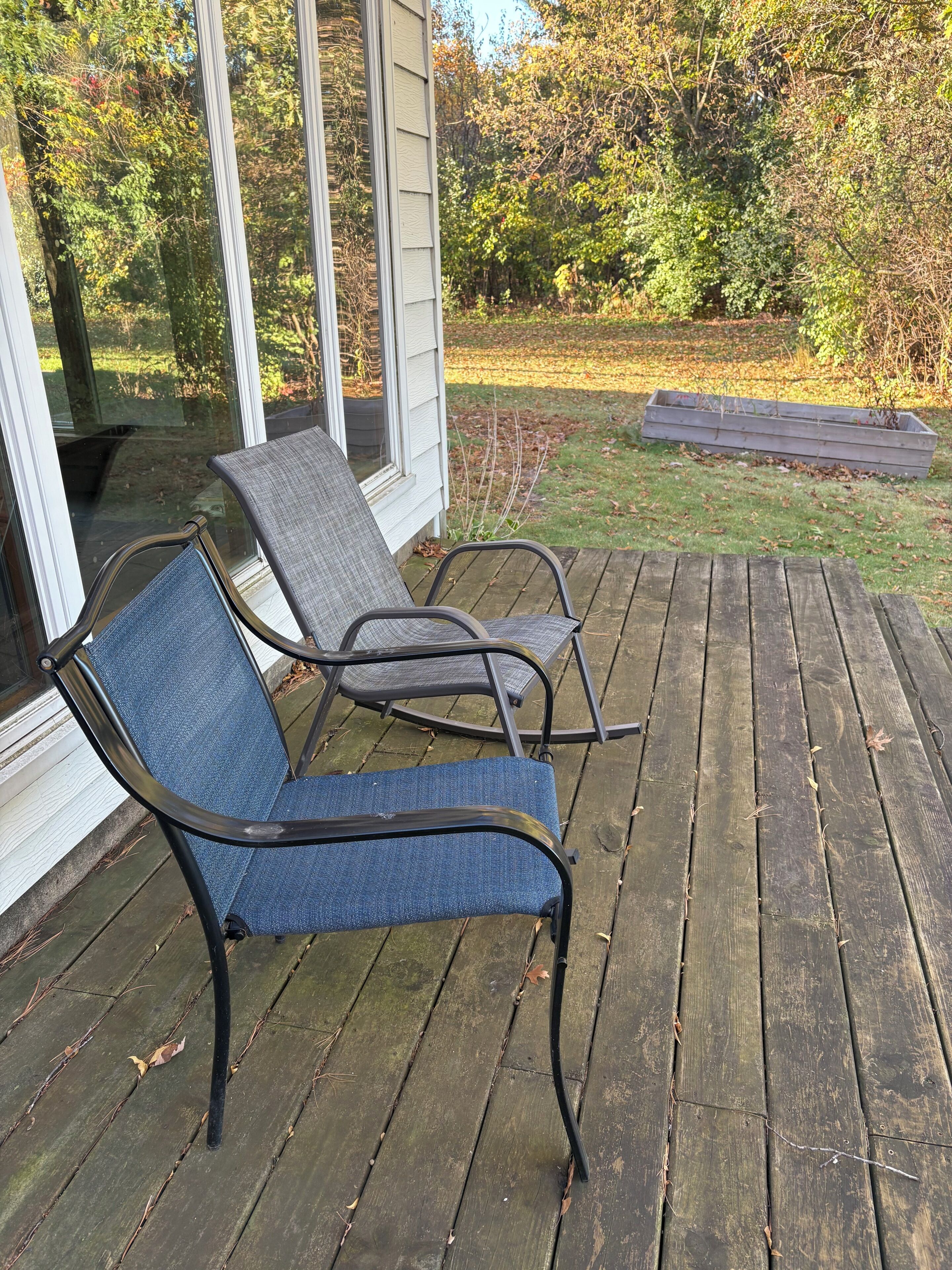Een houten terras met twee metalen stoelen en een bloembak.