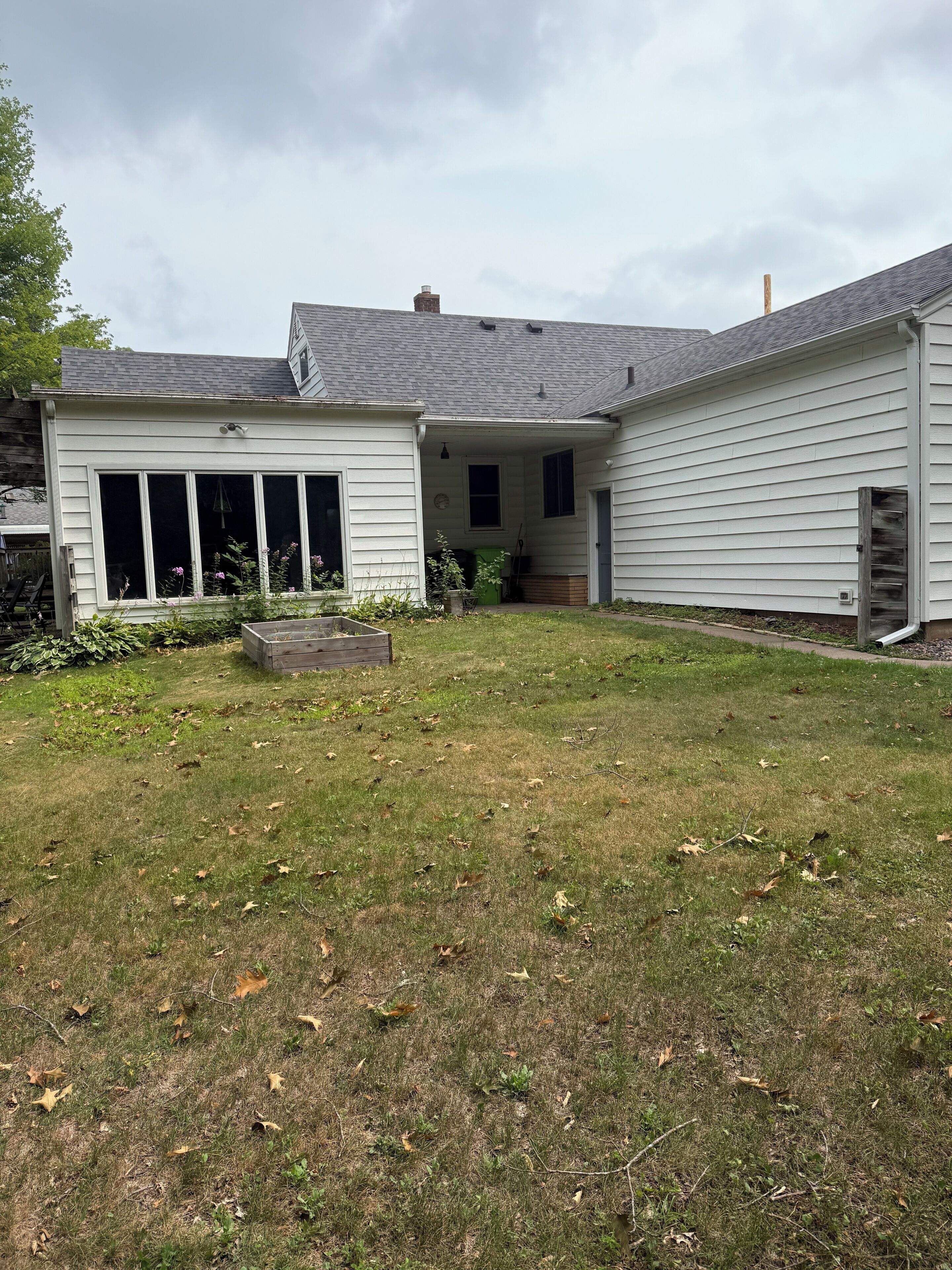 A residential property with a covered porch, a grassy yard, and a detached garage.