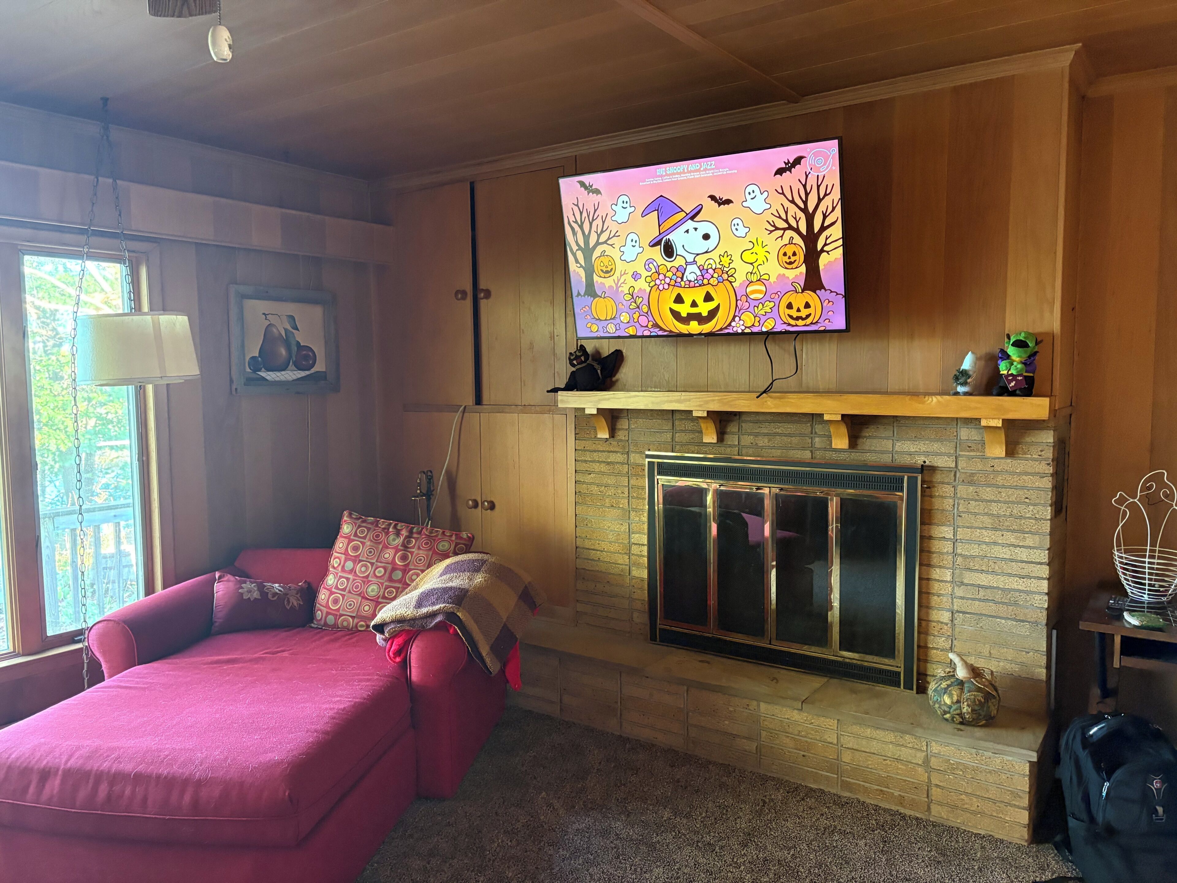 A cozy living room with a fireplace, a television mounted above it displaying a Halloween-themed image, and a comfortable red sofa.