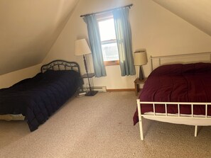 A bedroom with two beds, a window with curtains, a bedside table with a lamp, and a radiator.