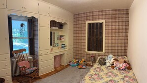 Quarto de criança com cama, cômoda, cadeira e janela com persianas.