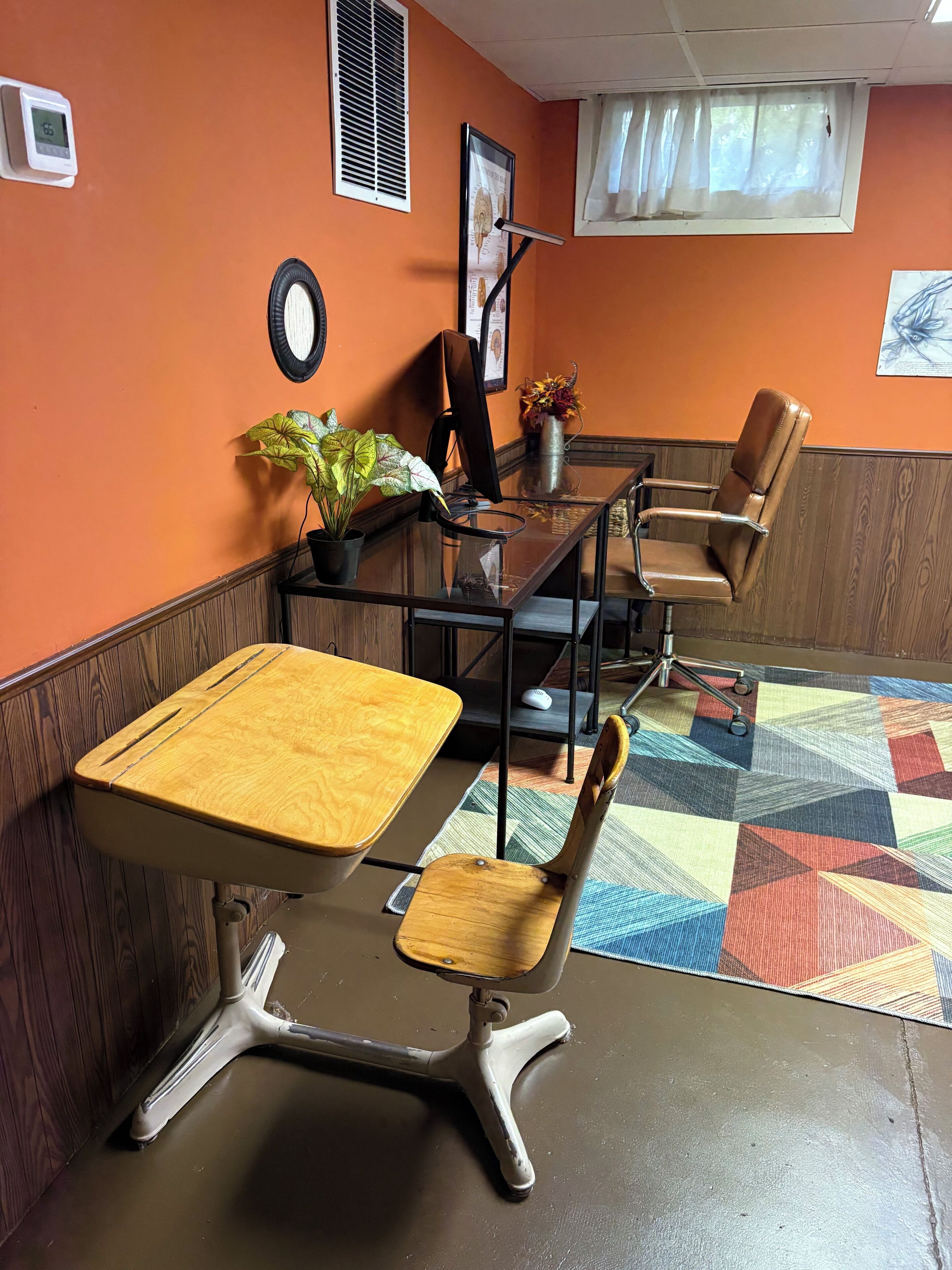 Een vergaderruimte met een glazen tafel, twee stoelen, een potplant en een wandklok.