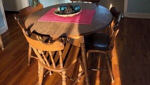 Uma área de refeições com uma mesa de madeira redonda, seis cadeiras, um jogo americano vermelho e duas decorações de parede.