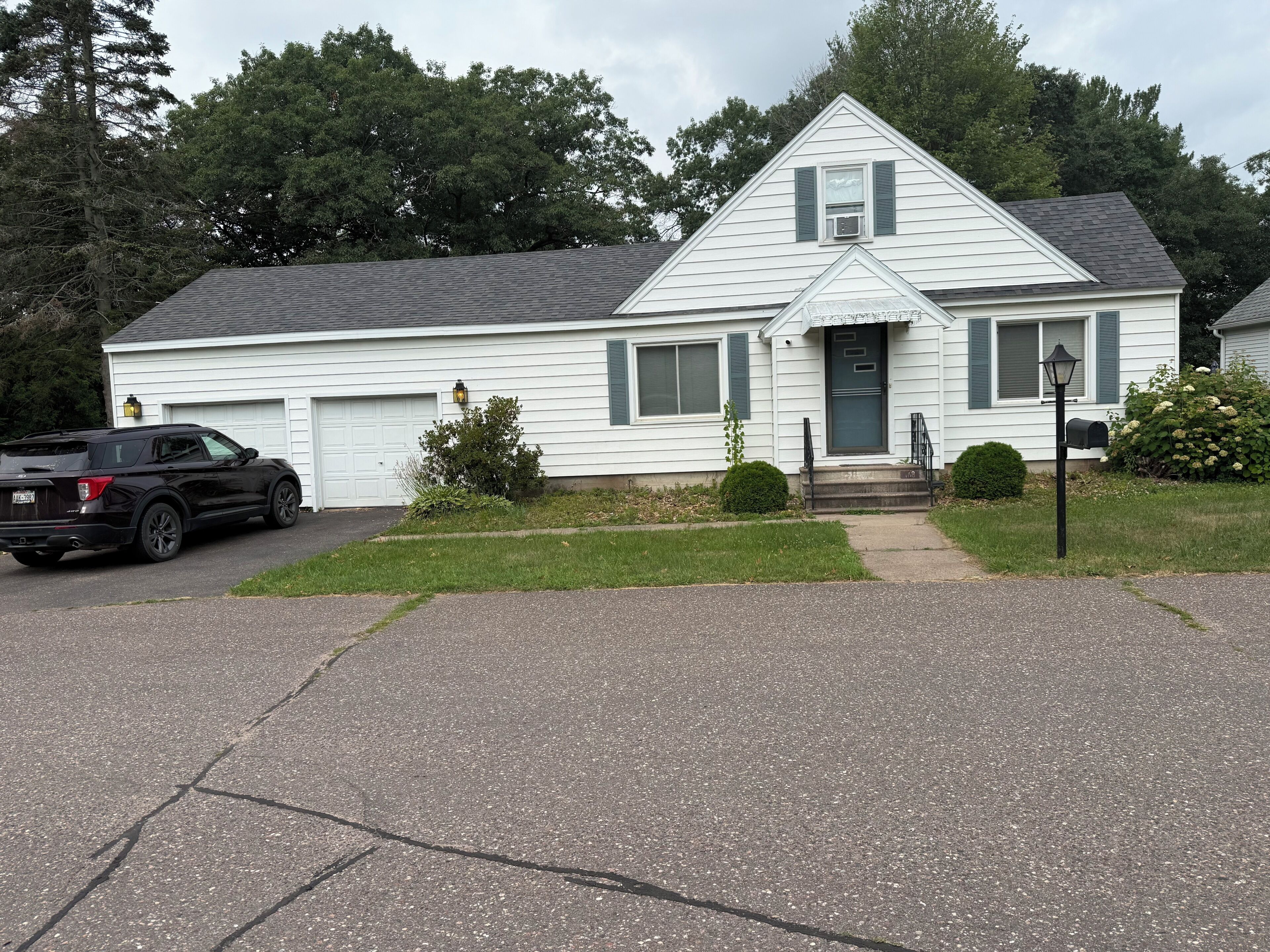 A two-story house with a garage, a driveway, and a black SUV parked in front.