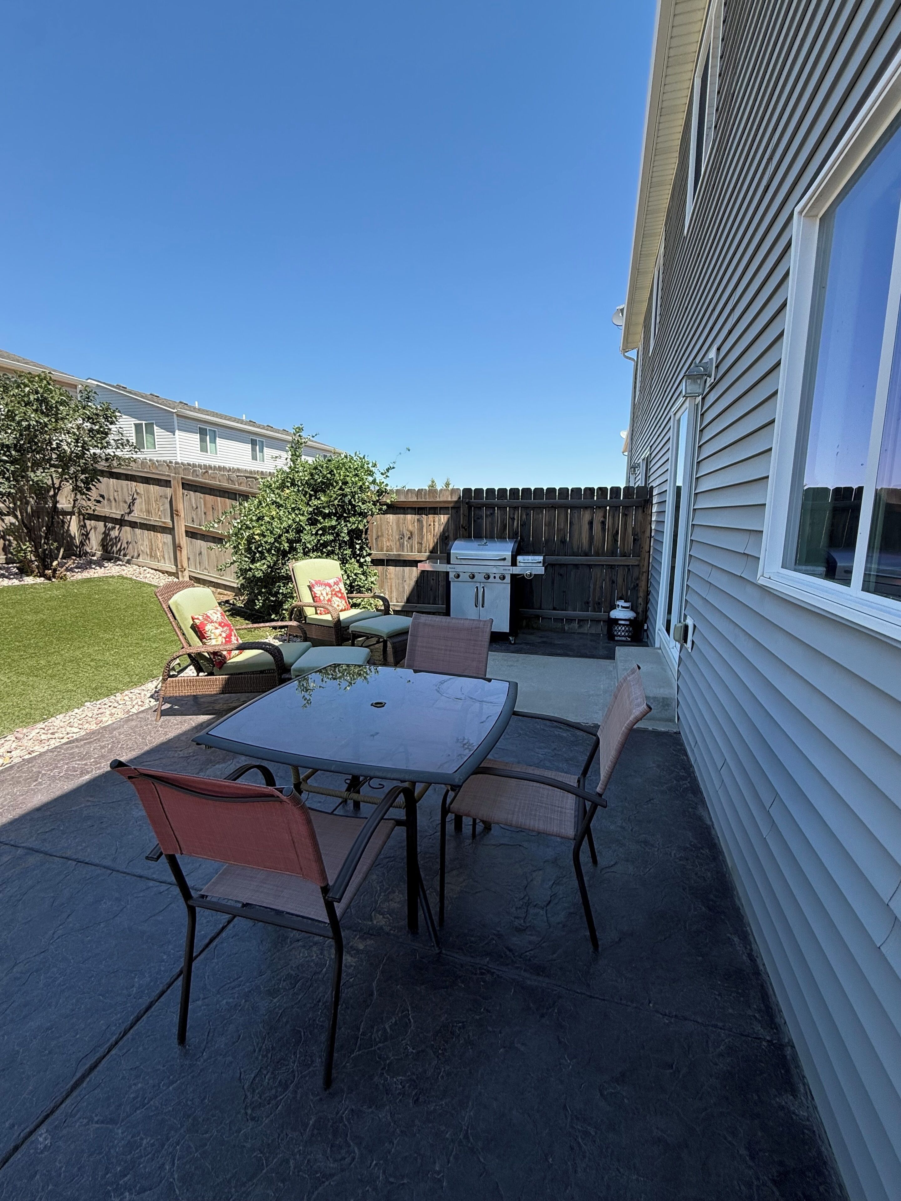 Un patio con mesa y sillas, una parrilla de barbacoa y un cerco de madera.