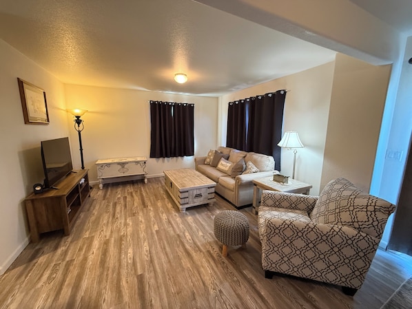 A living room with a sofa, ottoman, coffee table, TV, lamp, and curtains.