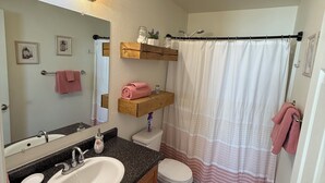 Ein Badezimmer mit Waschbecken, Spiegel, Handtuchhalter, Duschvorhang und einem Holzregal.