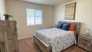 Ein Schlafzimmer mit Bett, Nachttisch, Kommode, Fenster und Deckenleuchte.