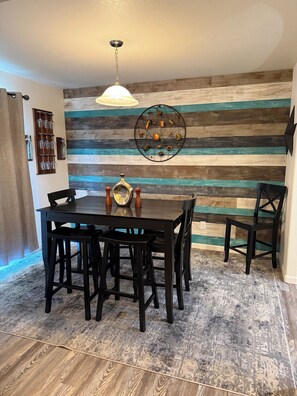 Een eethoek met een wand van houten planken, een ronde tafel met stoelen en een hanglamp.
