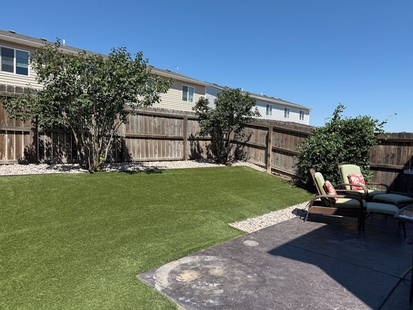 Un patio trasero con cerco de madera, césped y mobiliario exterior.