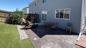 Ein wohnlicher Hinterhof mit Terrasse, Sitzgelegenheiten, Grill und Holzlattenzaun.