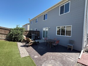 Een achtertuin met terras, tuinmeubels, een barbecue en een houten schutting.