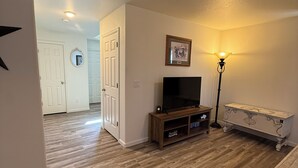 A living room with a wooden floor, a television on a wooden stand, a lamp, and a white couch.