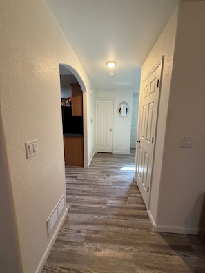 A hallway with a wooden floor, white walls, and a door at the end.