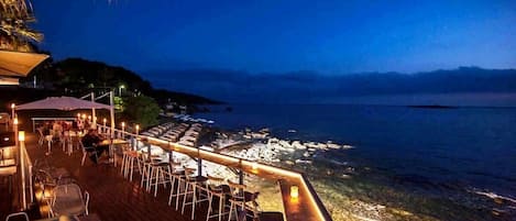A waterfront bar with outdoor seating overlooking the sea.