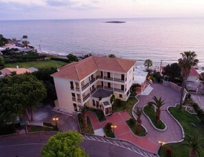 Un hotel de varios pisos con techo de tejas rojas, rodeado de palmeras y vistas al mar.