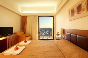 Una habitación de hotel con una cama, televisión, sofá, balcón con vistas y un cuadro en la pared.