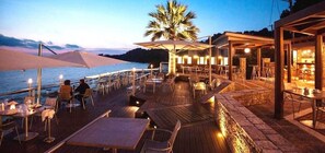 Un área de comedor al aire libre con mesas y sillas, una palmera y vista al mar.