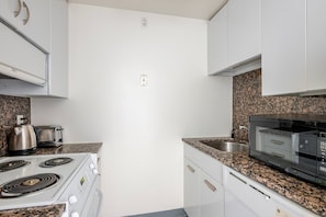 A kitchen with white cabinets, granite countertops, a stove, a kettle, a toaster, and a microwave. - Blueground | Prudential / St. Botolph, view, nr Boston Public Garden (Boston)