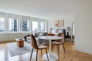 A modern hotel room with a large window, a sofa, a dining table with chairs, and a bed. - Blueground | Prudential / St. Botolph, view, nr Boston Public Garden (Boston)