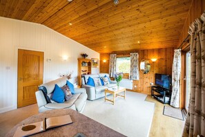 A cozy living room with a wooden ceiling, a sofa set, a coffee table, a television, and a bookshelf. - The Raven (Crianlarich)