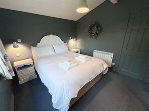 A neatly made bed with white linens and towels, a bedside table with a lamp, and a wall-mounted light fixture. - The Lapwing (Crianlarich)